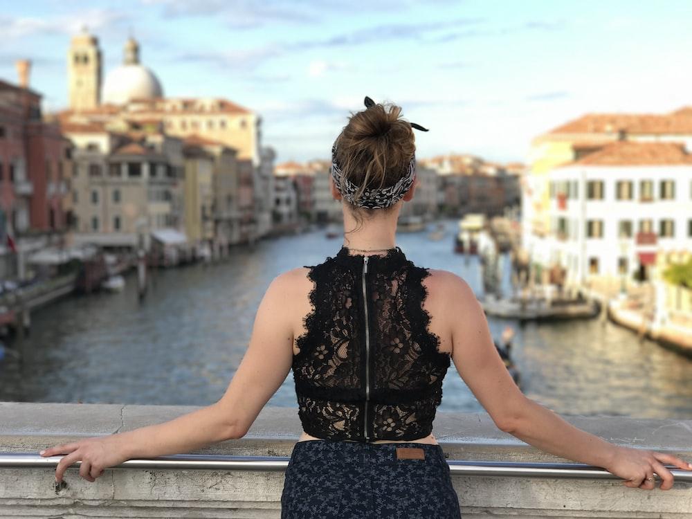 selective focus photography of woman holding gray metal handrail over body of water during daytime